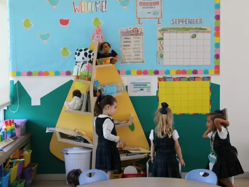 Aula de primaria con estudiantes explorando una estructura amarilla en forma de pirámide para lectura, con cartel "WELCOME" y calendario de septiembre.